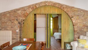 Una habitación rústica con una mesa de madera, sillas, una cama y una pared de ladrillo abovedada.