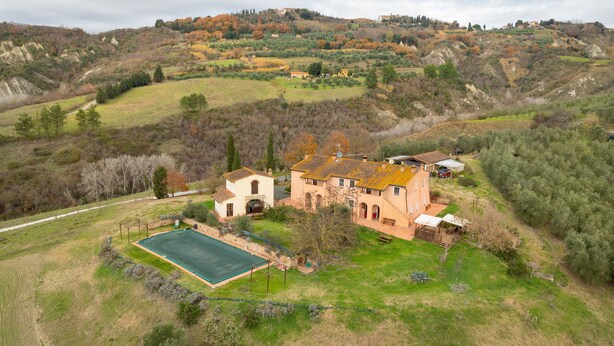 Una casa grande con cancha de tenis, rodeada de colinas y árboles.