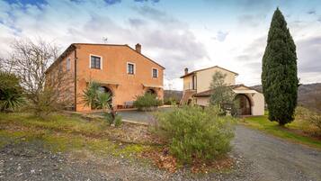 A two-story house with a gravel driveway, a tall cypress tree, and a clear sky.