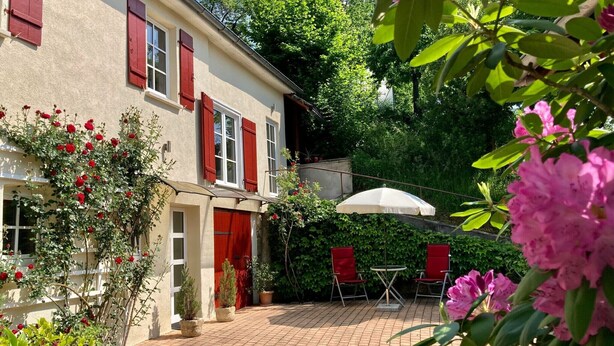 A courtyard with a brick floor, a white umbrella, red chairs, and potted plants.
