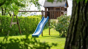 A playground with a slide, a wooden swing set, and a playhouse in a grassy area with trees. - Apartment Casa 'Bianca' with Wi-Fi and Air Conditioning (Novara)