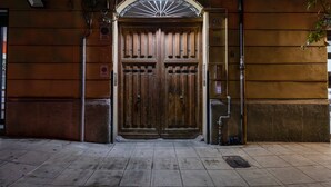 A large wooden double door with a metal arch above it, a sign on the right, and a suitcase on the ground.