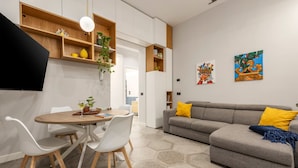 A modern living room with a grey sofa, white chairs, a wooden dining table, and hexagonal patterned flooring.