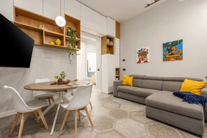 Een moderne woonkamer met een grijze bank, witte stoelen, een houten eettafel en vloerbekleding met een honingraatpatroon.