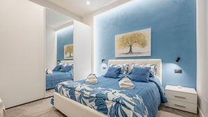 A bedroom with a large bed, a nightstand, a mirror, and a wall painting.