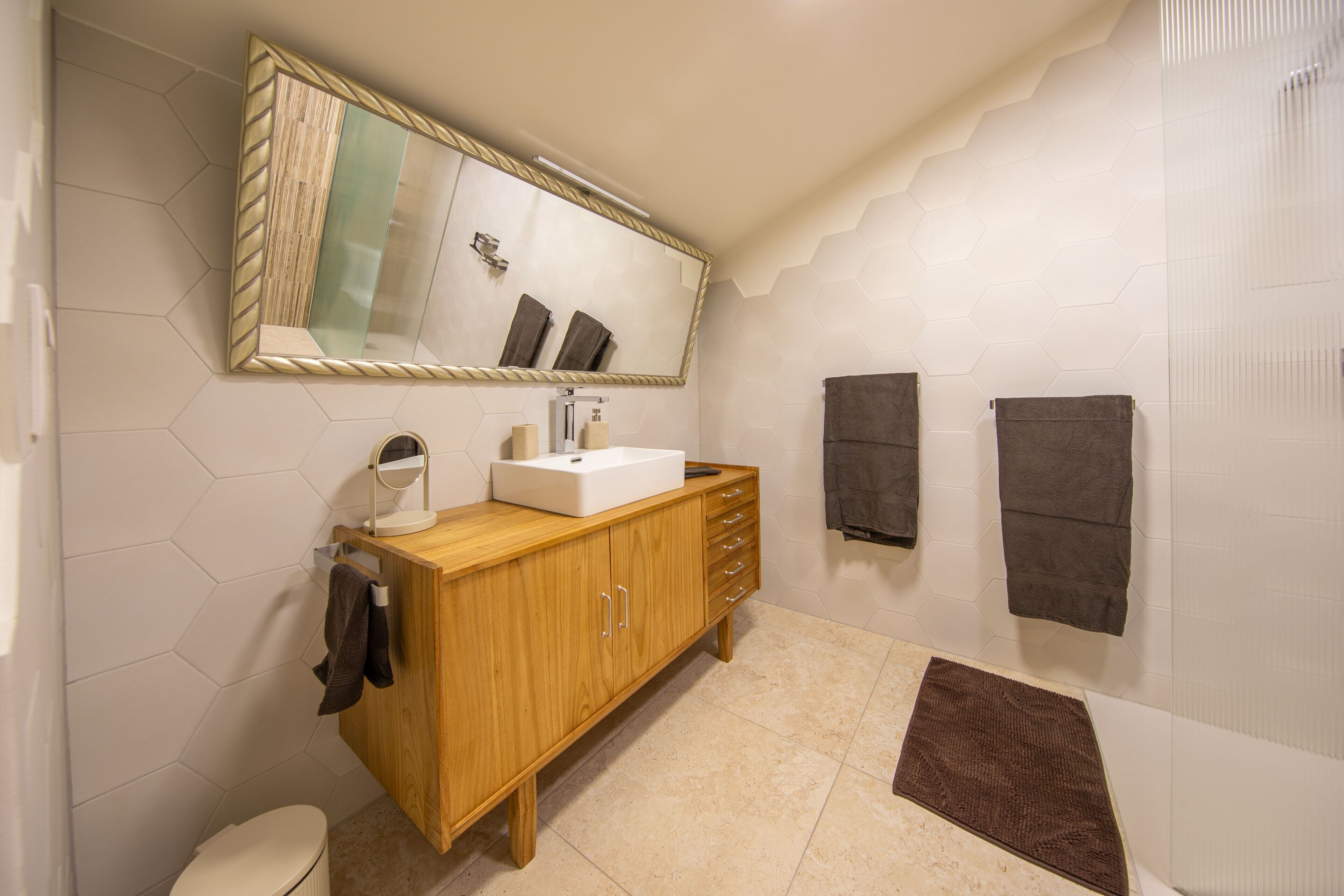 A bathroom with a wooden vanity, a large mirror, a toilet, and two towels hanging on the wall.
