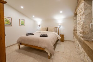 A bedroom with a bed, two wall-mounted lamps, a stone wall, and a door. - Holiday Home 'Gite Coeur Des Ondes - Tournesol' with Shared Terrace, Shared Garden and Wi-Fi (Saint-Georges)