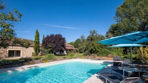 A swimming pool with lounge chairs and umbrellas, surrounded by stone buildings and greenery. - Holiday Home 'Gite Coeur Des Ondes - Tournesol' with Shared Terrace, Shared Garden and Wi-Fi (Saint-Georges)
