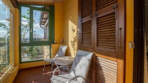 Un balcón con vistas, sillas de mimbre y contraventanas de madera.