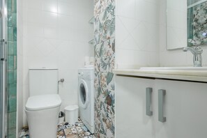 Et badeværelse med toilet, vaskemaskine og et håndvaskspejl.