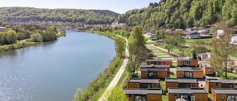 A riverside view of a hotel with modern cabins, a clear sky, and surrounding greenery.
