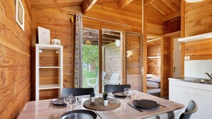 Interior d'una cabana de fusta amb taula de dinar preparada per a quatre persones, zona de cuina i porta corredissa de vidre que dona a una zona d'estar a l'aire lliure.