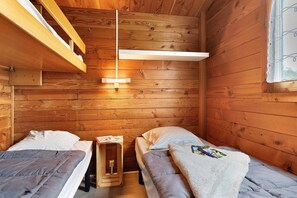 A wooden cabin room with two beds, a small table, and a hanging light fixture.