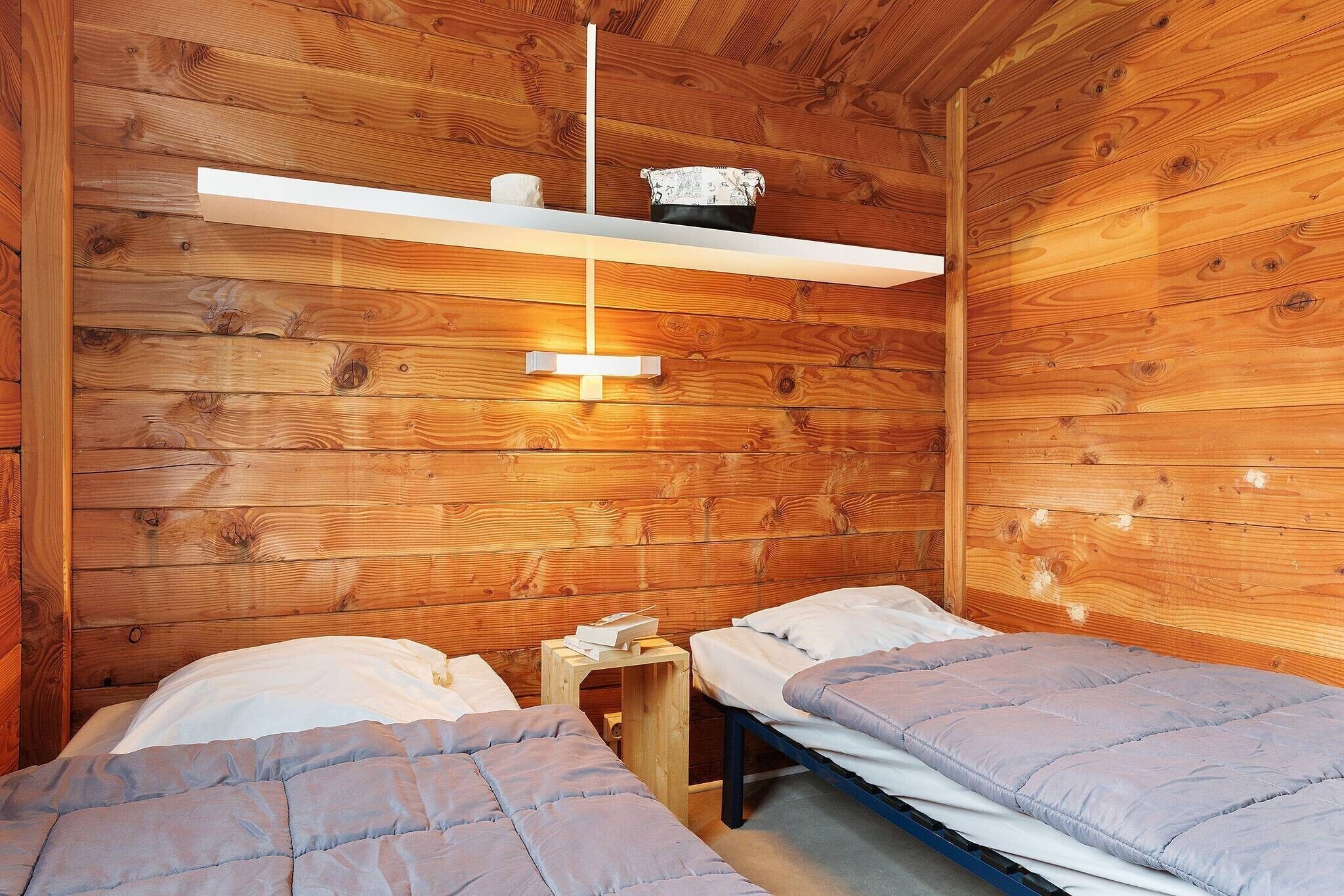 Une pièce de cabane en bois comprenant deux lits, une étagère avec un luminaire et une petite table.