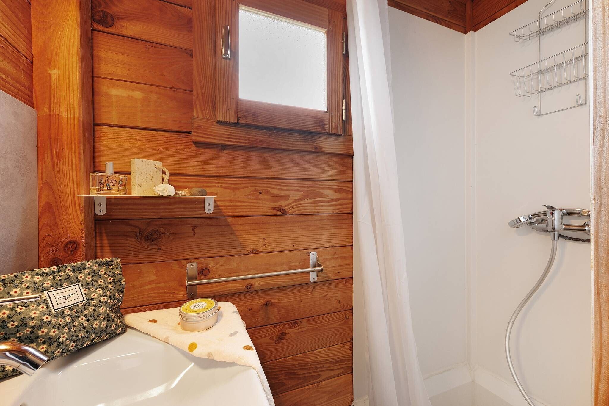 A wooden cabin bathroom with a sink, a towel rack, a shower, and a window.