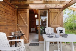 A wooden cabin with a dining area featuring a table, chairs, and a grill.