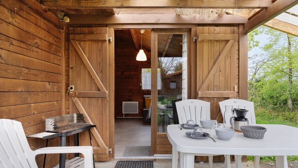 Une cabane en bois dotée d’un coin repas comprenant une table, des chaises et un barbecue.