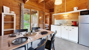 L’intérieur d’un chalet en bois, avec une table à manger, un coin cuisine et une vue à travers une porte vitrée.