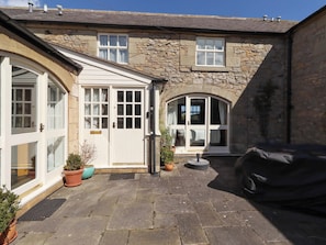 A stone building with a covered patio, a door, and potted plants. - 3 Christon Bank Mews (Alnwick)