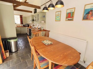 A kitchen with a dining table, chairs, and a radiator. There are cabinets, a sink, and a window with curtains. - 3 Christon Bank Mews (Alnwick)
