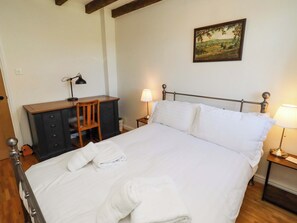 A neatly made bed with white linens, a wooden desk with a chair, a lamp, and a painting on the wall. - 3 Christon Bank Mews (Alnwick)