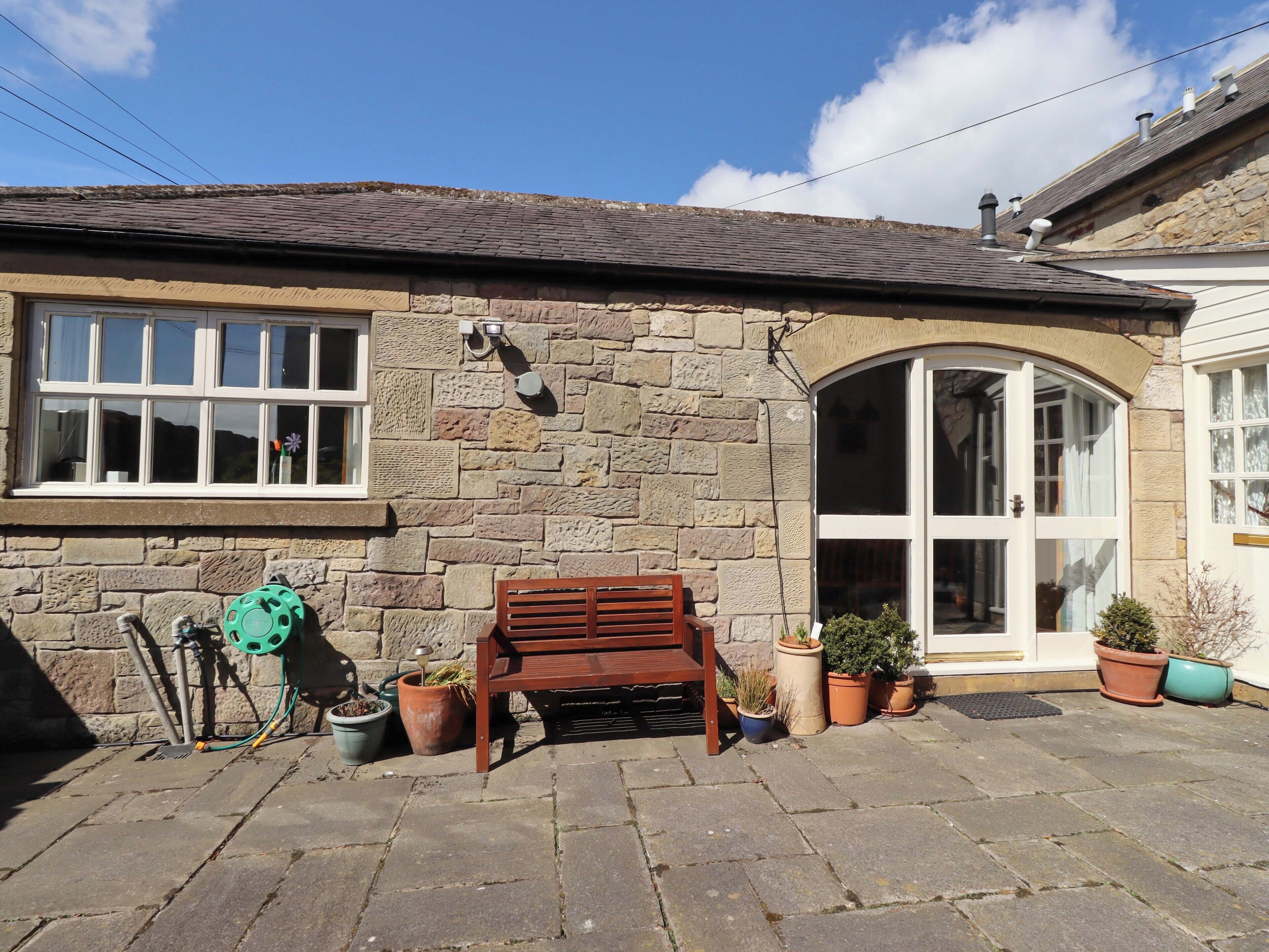 A stone building with a tiled roof, a wooden bench, and potted plants.