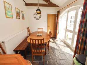 A dining area with a round wooden table, chairs, a bench, a wall clock, framed pictures, and a window with curtains. - 3 Christon Bank Mews (Alnwick)