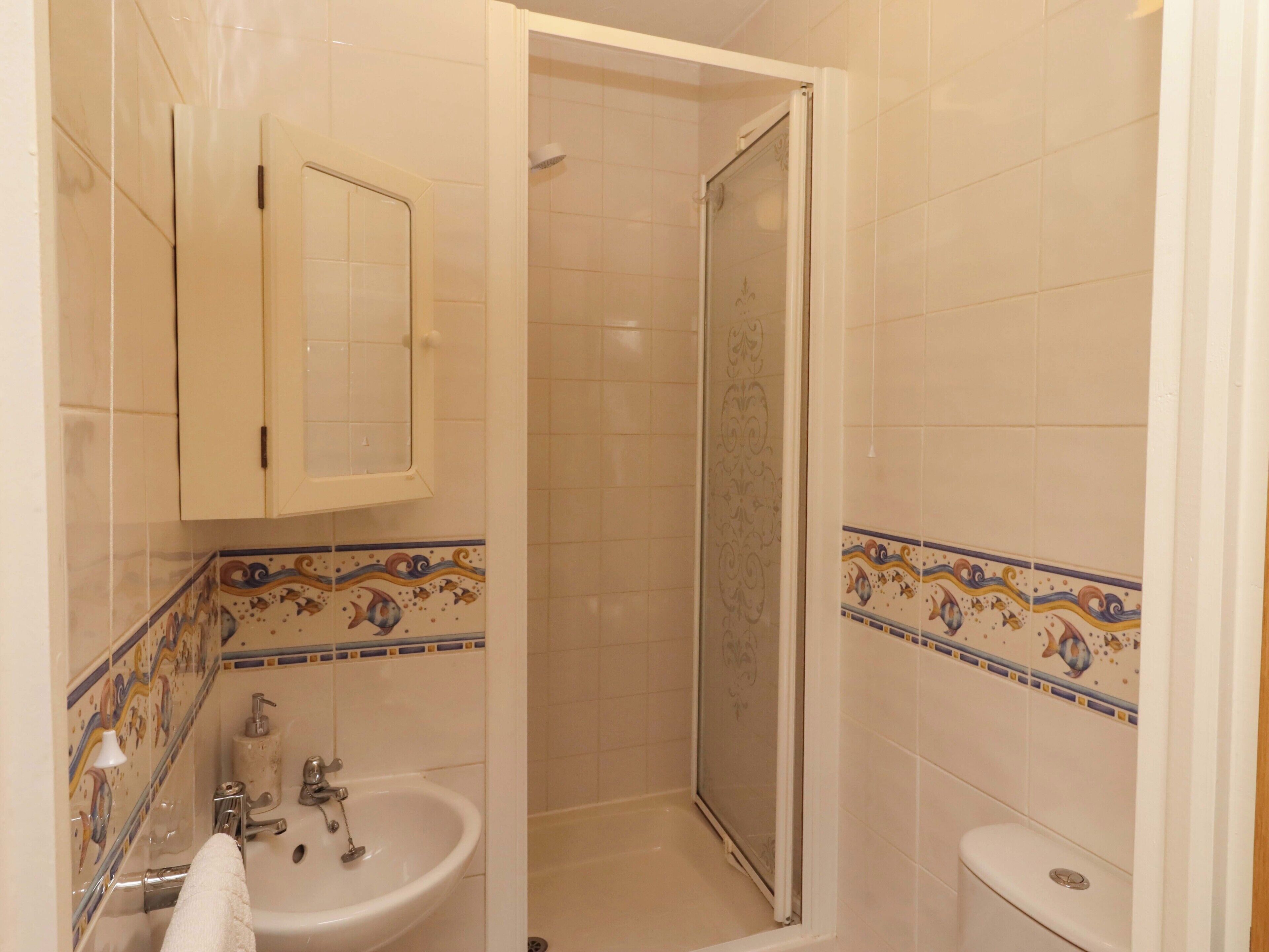 Een badkamer met een douche, wastafel, toilet en kast.