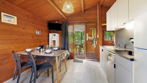 A wooden interior with a dining table, chairs, a kitchen area, and a view through a doorway. - Chalet “Prestige Le 13” with Shared Pool, Communal Garden and Wi-Fi (Saint-Gervais)