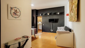 A living room with a glass coffee table, a sofa, a TV mounted on the wall, and a radiator.