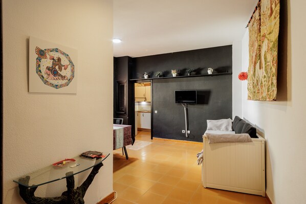 A living room with a glass coffee table, a sofa, a TV mounted on the wall, and a radiator.