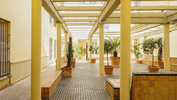 A covered outdoor area with tiled flooring, yellow columns, and potted plants.