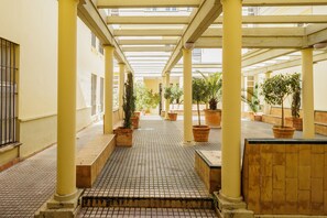 Un espace extérieur abrité, doté d’un sol carrelé, de colonnes jaunes et de plantes en pot.