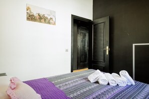 A room with a bed, a black door, a white wall, and a framed picture.