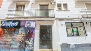 Un edificio con una tienda cerrada en la planta baja, un balcón con barandilla metálica y una ventana con un cartel arriba.