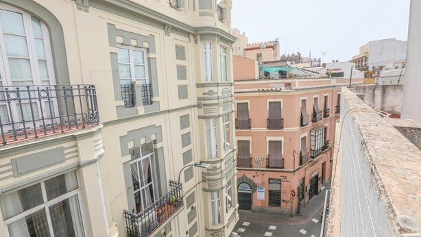 Un edificio de varios pisos con balcones, vista a la calle y una tienda con rótulos.