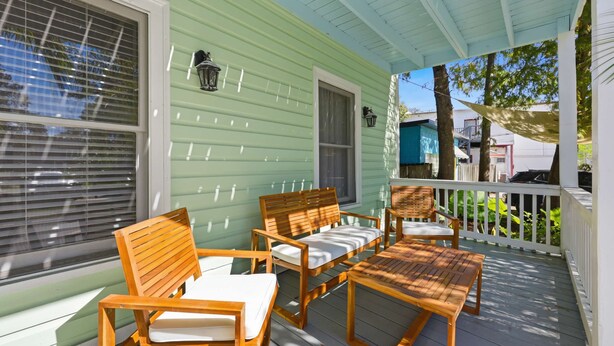 A covered porch with wooden furniture, including chairs and a table, and a green exterior wall. - The Pearl, 2 Unit Stay for 10 (St. Augustine)