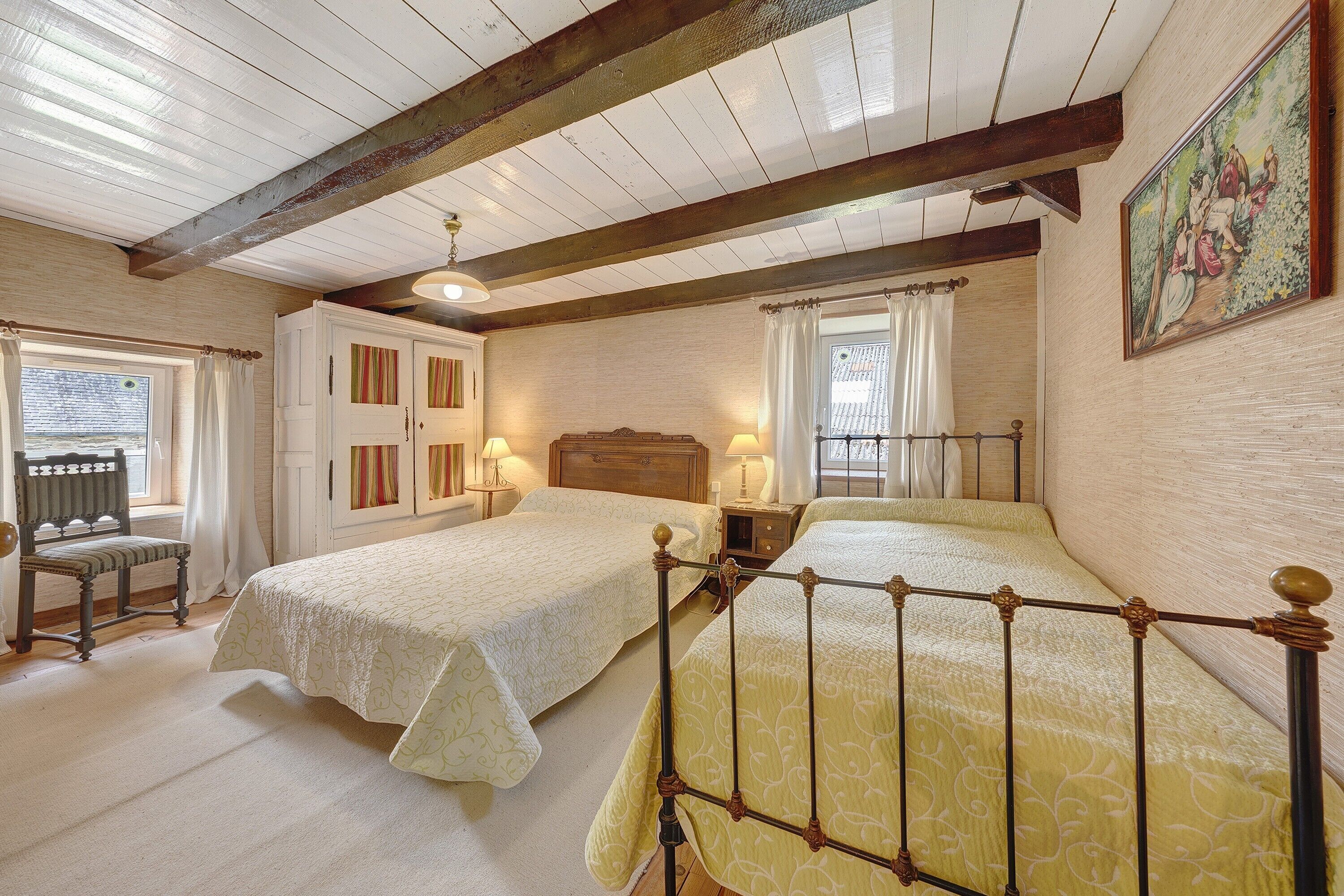 Ein Schlafzimmer mit zwei Betten, einem Holzstuhl, einem Nachttisch und einem Bild an der Wand.