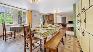 Un coin repas avec une table dressée pour quatre personnes, des chaises en bois, un banc et une cuisine en arrière-plan.