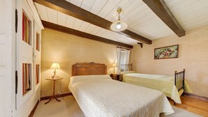 Une chambre avec deux lits, un plafond en bois, une petite table avec une lampe et un tableau au mur.