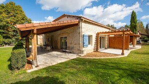 Une maison en pierre dotée d’un patio couvert, d’une pergola en bois et d’une pelouse bien entretenue.