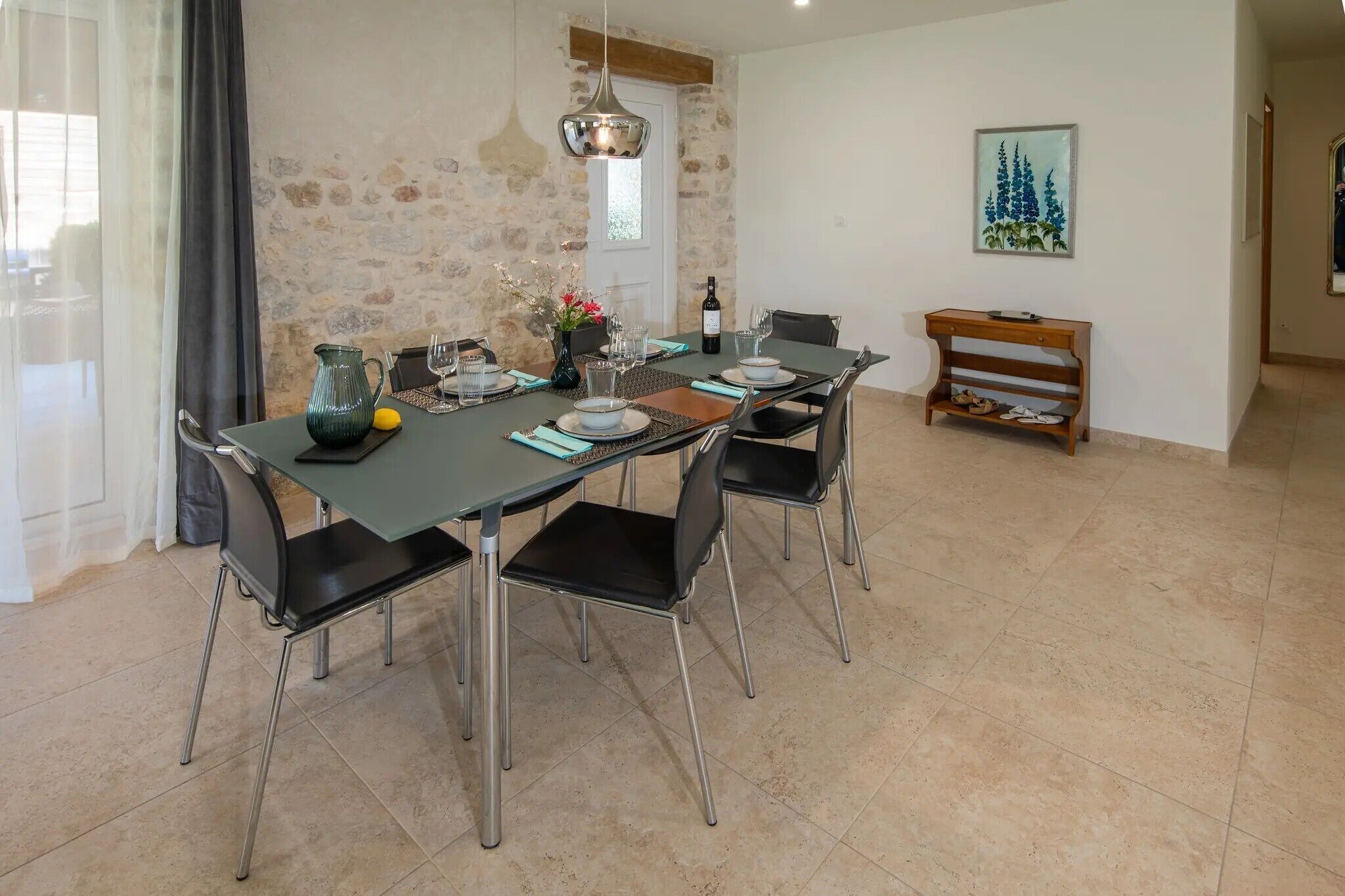 A dining area with a table set for four, chairs, a bench, a vase with flowers, and a bottle of wine.