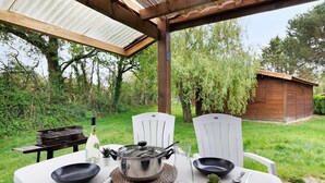 An outdoor dining area with a table set for two, a grill, and a wooden structure in the background. - Chalet "Confort 16" with Terrace and Shared Pool (Saint-Gervais)