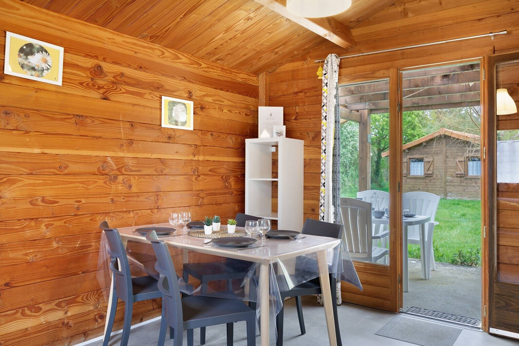 A wooden cabin with a dining table set for four, a white cabinet, and a sliding glass door leading to an outdoor area.