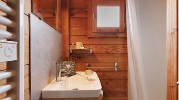 A wooden cabin bathroom with a white sink, a small window, and a towel rack.