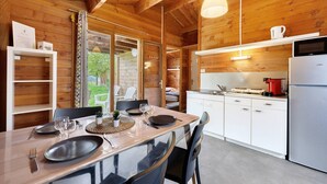 A wooden interior with a dining table set for four, a kitchen area with a refrigerator, and a view of the outdoors. - Chalet "Confort 11" with Terrace and Shared Pool (Saint-Gervais)