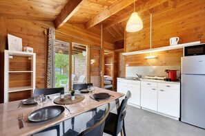 A wooden interior with a dining table set for four, a kitchen area with a refrigerator, and a view of the outdoors. - Chalet "Confort 11" with Terrace and Shared Pool (Saint-Gervais)