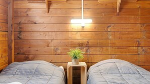 Ein Zimmer in einer Holzhütte mit zwei Betten, einem kleinen Tisch mit einer Pflanze und einer Hängelampe.
