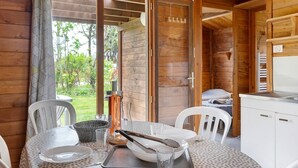 Ein Interieur einer Holzhütte mit Esstisch für zwei Personen, einer Küchenzeile und einer Glasschiebetür, die zu einem Garten führt.