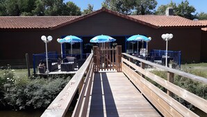 Een houten terras dat leidt naar een gebouw met blauwe parasols en terrasstoelen.